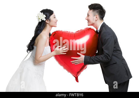 Glückliche Braut und Bräutigam halten einen herzförmigen Ballon Stockfoto