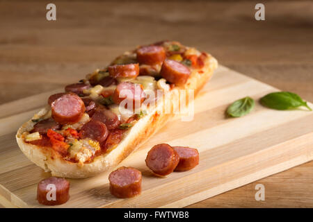 Pizza-Baguette, gefüllt mit Wurst auf Holzbrett Stockfoto