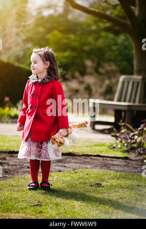 ein verlorene kleine Mädchen tragen roten Mantel stehen im Park hält eine Spielzeug Stockfoto