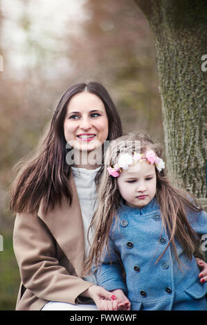 junge Frau mit ihrer kleinen Tochter unter dem Baum sitzt Stockfoto