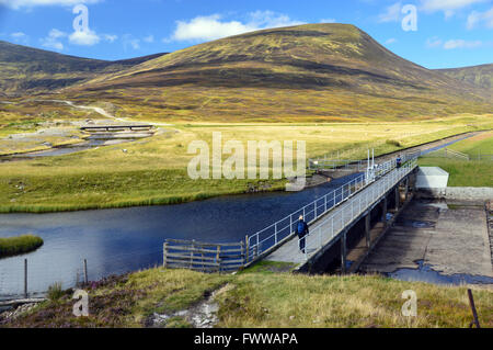 Eine Frau, die zu Fuß über den Abfluss von Loch Garry unter den Corbett eingestuft Scottish Mountain, die Sau von Atholl. Stockfoto