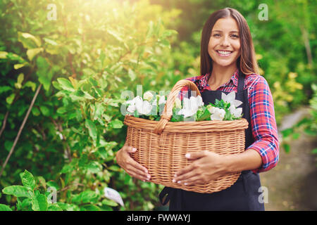 Glückliche Frau genießen ihre Arbeit im Kindergarten stehen draußen in einem Garten umklammert einen Weidenkorb voller frische weiße Blumen Stockfoto