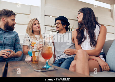 Gruppe junger Menschen sitzen um einen Tisch im Chat. Junge Freunde zusammen feiern, mit Cocktails am Tisch. Stockfoto