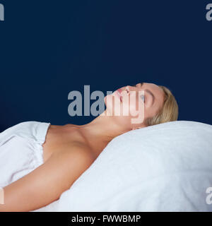 Innenaufnahme der attraktiven jungen Frau, die auf Massagetisch liegen. Kaukasische Frau eingehüllt in weißen Handtuch auf Bett wegsehen. Stockfoto