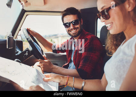 Junges Paar sitzt in ihrem Auto mit Karte. Lächelnder junger Mann und Frau zusammen zu sitzen und mit Blick auf die Karte für directio Stockfoto