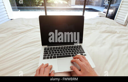 Nahaufnahme Bild der Frau auf einem Bett auf Laptop-Computer arbeiten. POV Aufnahme Frau entspannend im Schlafzimmer mit Laptop. Stockfoto