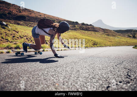 Heckansicht des jungen Frau üben Skateboarden auf der Landstraße an Sommertag. Sie ist die Straße berühren, dabei Stunts. Stockfoto