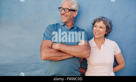 Portrait über ein älteres paar zusammenstehen und wegsehen und lächelnd vor blauem Hintergrund. Mittleren Alter Mann und Frau le Stockfoto