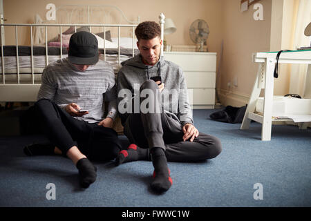 Zwei männliche Studenten im Schlafzimmer überprüfen Sie Nachrichten auf dem Handy Stockfoto