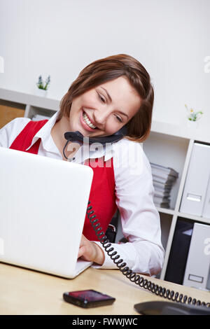 Lächelnde Studentin am Schreibtisch mit Laptop-Computer mit Handy Stockfoto