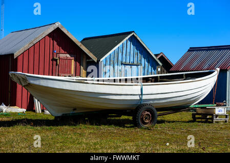 Simrishamn, Schweden - 1. April 2016: Weiße traditionelle Jagd Kanu auf einem Anhänger vor roten und blauen Fischerhütten. Stockfoto