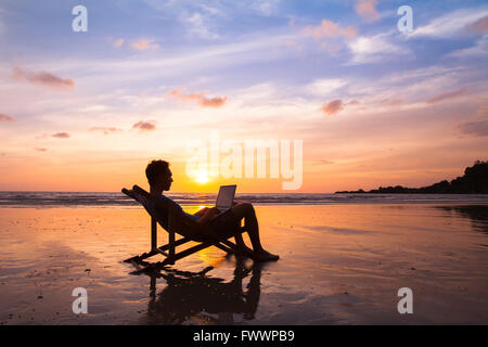 Silhouette des glücklichen Geschäftsmann mit Laptop arbeiten am Strand Stockfoto