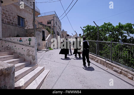 Jerusalem, Israel. April 2016. Zwei ultra-orthodoxe religiöse Juden werden von zwei bewaffneten Sicherheitsleuten durch das palästinensische Viertel Silwan oder Siloam begleitet, das sich an den Hängen südlich der alten Stadtmauer in Ostjerusalem Israel befindet Stockfoto