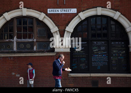 Ein Mann Essen einen Snack vorbei an der Boleyn Taverne an der Green Street, nahe Boleyn Ground vor West Ham United, Crystal Palace in eine Barclays Premier League gehostet übereinstimmen. Die Boleyn Ground im Upton Park war der Club Heimstadion von 1904 bis zum Ende der Saison 2015 / 16 in das Olympiastadion für die Spiele 2012 in London, in der Nähe Stratford gebaut zog. Das Spiel endete mit einem 2: 2 Unentschieden, beobachtet von einem in der Nähe von ausverkauftem von 34.857. Stockfoto