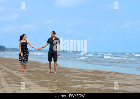Paar am Strand spazieren. Junge glückliche interracial paar zu Fuß am Strand und lächelnd zu einander. Asiatische Frau, kaukasischen Mann Stockfoto