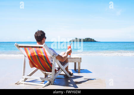 Mann entspannen am Privatstrand auf Trauminsel, luxuriöser Urlaub, Touristen mit cocktail sitzen in der Nähe des Meeres Stockfoto