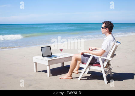 Telearbeit, Geschäftsmann, entspannen am Strand mit Laptop und cocktail, freier Mitarbeiter am Arbeitsplatz, Traumjob Stockfoto