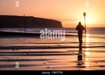 Ein Mann geht auf Sandown Strand bei Sonnenaufgang Stockfoto