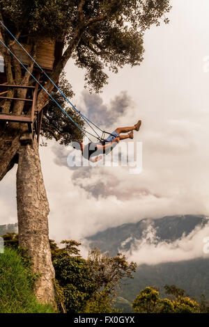 Silhouette der entspannenden Teenager Mann auf einer Schaukel, Casa Del Arbol, Baumhaus, Vulkan Tungurahua mächtige Explosion Stockfoto