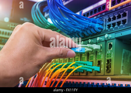 Hand mit LWL-Netzwerkkabel an Server in einem Rechenzentrum angeschlossen Stockfoto
