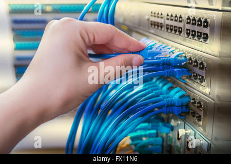 Hand mit Netzwerkkabel verbunden zu Servern in einem Rechenzentrum Stockfoto