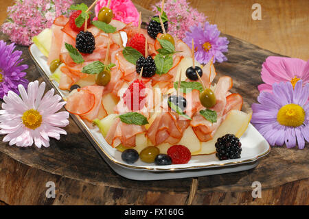 Galia-Melone mit Schinken, garniert mit Himbeeren, Heidelbeeren, Brombeeren und Oliven auf einer Platte Stockfoto