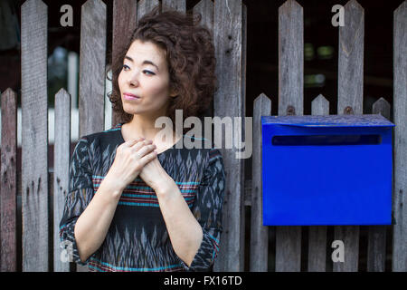 Asiatische Frau steht in der Nähe des Zauns mit einem blauen Postfach. Stockfoto