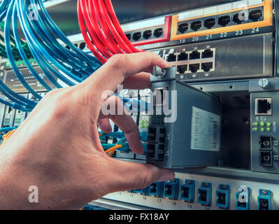 Hand mit LWL-Netzwerkkabel an Server in einem Rechenzentrum angeschlossen Stockfoto