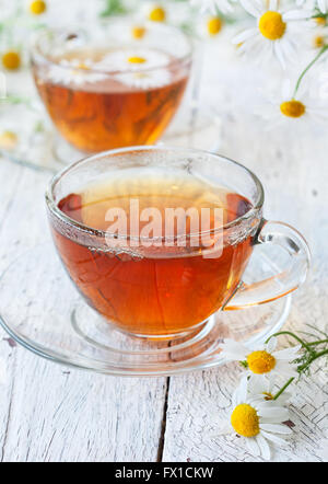 Kamillentee in Tassen aus Glas, ein Bouquet von Kamillen auf weißem Holz Hintergrund Stockfoto