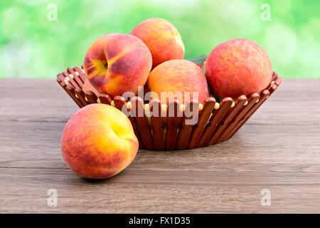 Reife Pfirsiche in Korb auf grünem Hintergrund Stockfoto