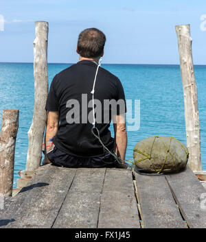 Ein Mann sitzt auf einem Pier mit einer Schlinge um den Hals Stockfoto