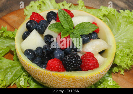 Melonen-Bits, Himbeeren, Brombeeren und Heidelbeeren in einer halbierten und ausgehöhlten Galia-Melone, garniert mit Minze Stockfoto