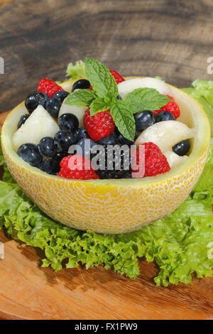 Melonen-Bits, Himbeeren, Brombeeren und Heidelbeeren in einer halbierten und ausgehöhlten Galia-Melone, garniert mit Minze Stockfoto