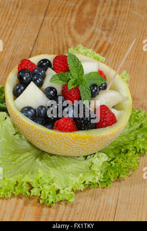 Melonen-Bits, Himbeeren, Brombeeren und Heidelbeeren in einer halbierten und ausgehöhlten Galia-Melone, garniert mit Minze Stockfoto