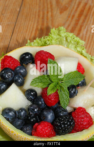 Melonen-Bits, Himbeeren, Brombeeren und Heidelbeeren in einer halbierten und ausgehöhlten Galia-Melone, garniert mit Minze Stockfoto