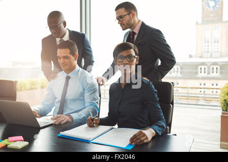 Attraktive Gruppe von vier Rassen junge Geschäftsleute am Konferenztisch mit Haftnotizen, Notizblock und offenen Laptop sitzen Stockfoto