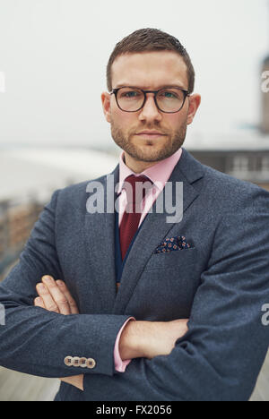 Ernst entschlossenen jungen Mann mit Brille steht mit verschränkten Armen in die Kamera schaut, mit einem nachdenklichen intensive exp Stockfoto