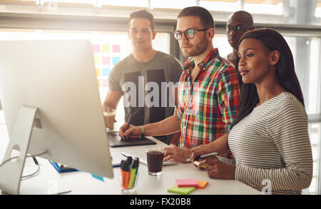 Gruppe von vier schwarzen, kaukasischen und hispanischen Erwachsenen Unternehmer tragen Freizeitkleidung stehend rund um Computer für Dämon Stockfoto