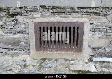 Nahaufnahme des alten, etwas rostig, Gusseisen Gitter oder Air Vent in eine Steinmauer. Stockfoto