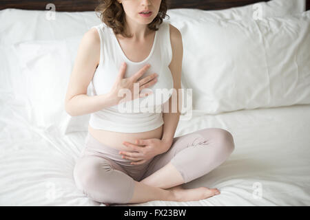 Nahaufnahme von jungen schwangeren Yoga-Übung zu tun. Weibliches Model auf dem Bett sitzt mit gekreuzten Beinen in einfach darstellen Stockfoto