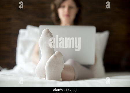 Schöne junge Frau sitzt auf Bett mit Laptop in modernen Zimmer. Kaukasische Modell entspannend mit Computer im Haus Stockfoto