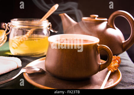 Eine Tasse heißen Tee auf einem Tisch mit Teekanne und Honig im Hintergrund Stockfoto