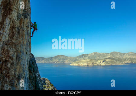 kleinen Kletterer auf steilen Felsen mit blauen Meer hinter Silhouette Stockfoto