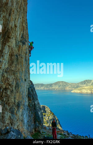 kleinen Kletterer auf steilen Felsen mit blauen Meer hinter Silhouette Stockfoto