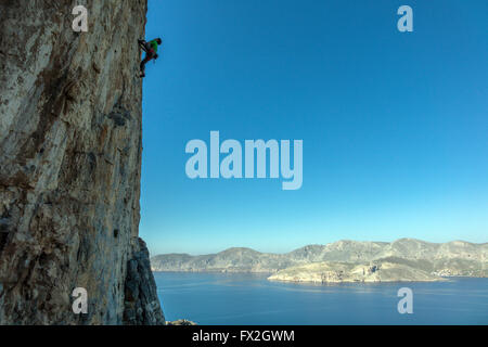 kleinen Kletterer auf steilen Felsen mit blauen Meer hinter Silhouette Stockfoto