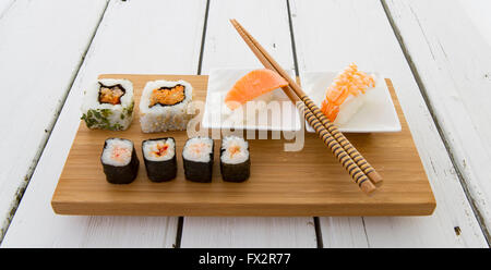 Sushi serviert auf einem Bambus-Brett mit Stäbchen auf einem rustikalen Holztisch weiß Stockfoto