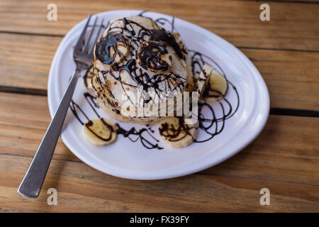 Stapel von Pfannkuchen in einem Restaurant mit Bananen und Schokoladensauce an der Spitze. Stockfoto