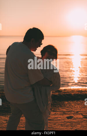 Erwachsenes paar umarmt bei Sonnenuntergang und Meer. Stockfoto