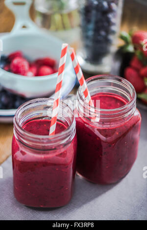 Zwei Gläser mit Beeren-Smoothie, frisches Obst im Hintergrund. Sauber Essen und Diät Konzept Stockfoto