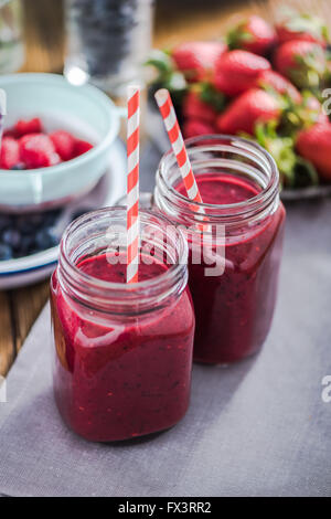 Zwei Gläser mit Beeren-Smoothie, frisches Obst im Hintergrund. Sauber Essen und Diät Konzept Stockfoto